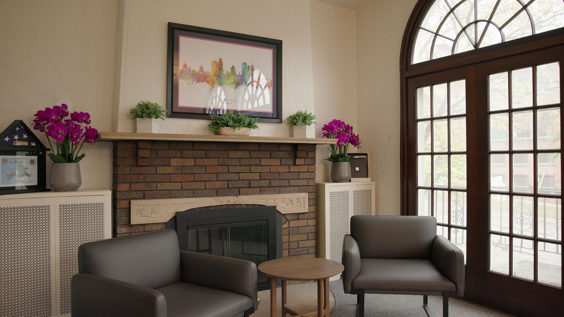 Cozy living room with fireplace, two armchairs, small table, and a large window.