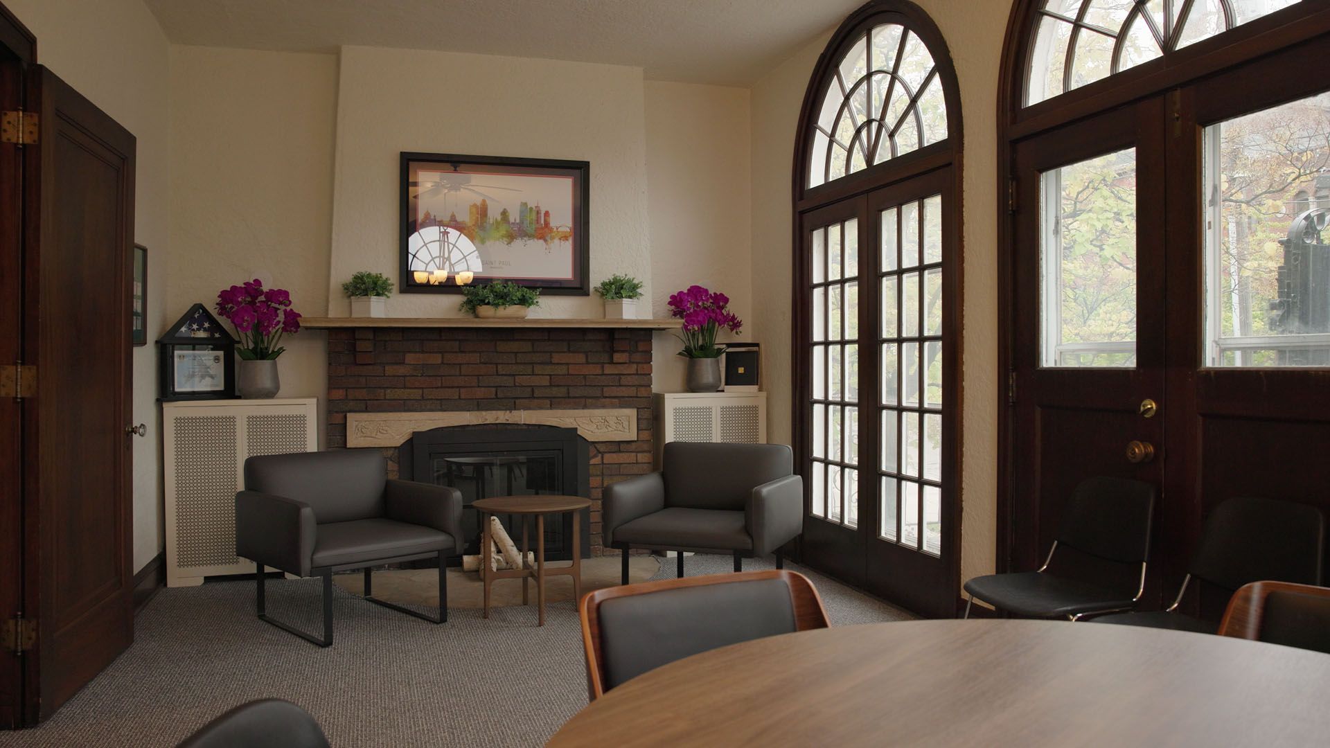 A living room with a fireplace, two armchairs, round table, and arched French doors.
