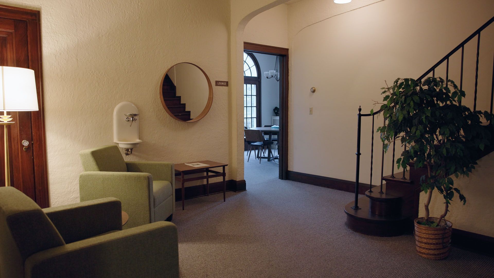 Waiting room with green chairs, round mirror, and stairs leading up.