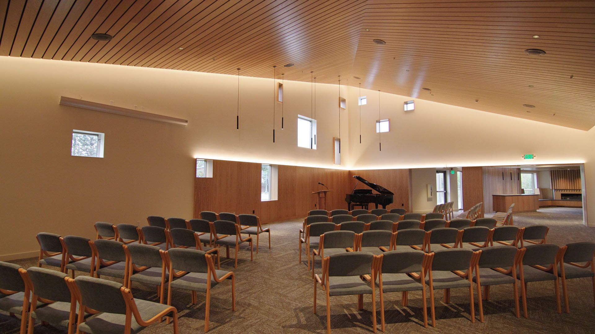 A modern, light-filled chapel with rows of chairs, a grand piano, and wood-paneled walls.