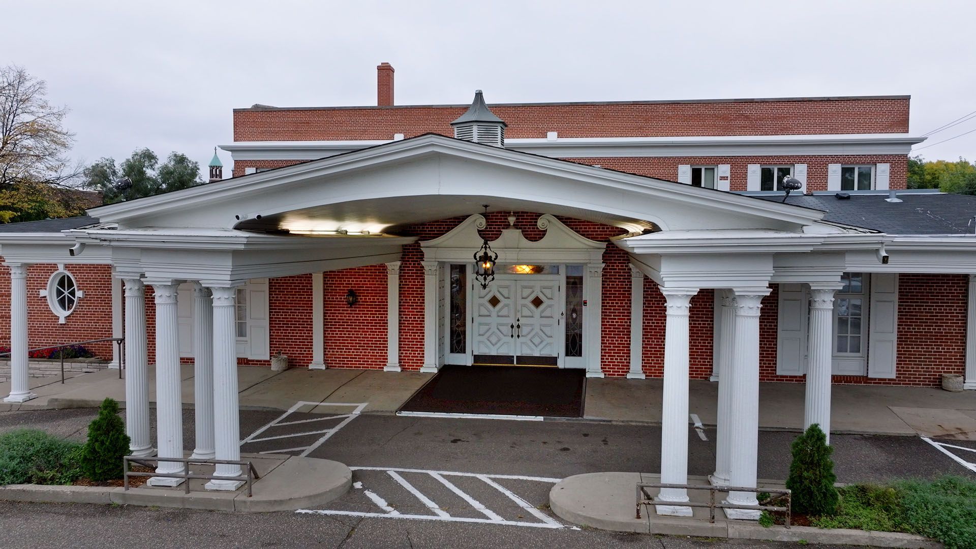 Red brick building with white columns and entrance canopy. Driveway in front.