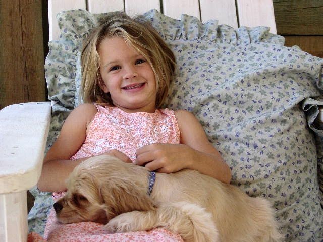 A little girl is laying in a chair with a Cocker Spaniel puppy on her lap