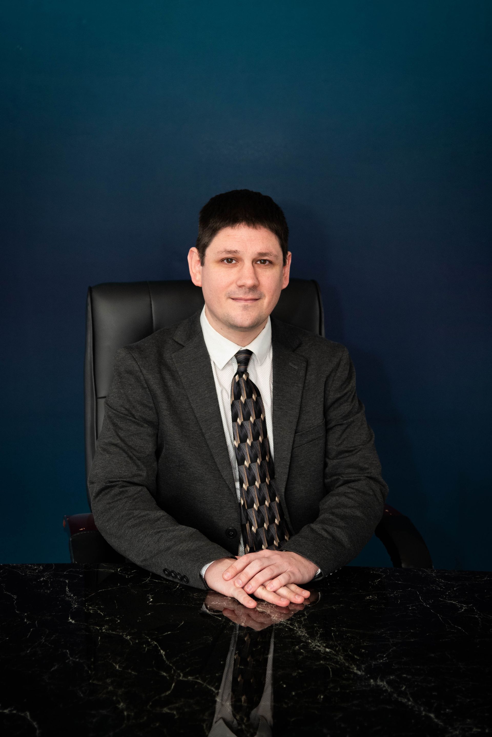 Man in blue suit and tie smiling, posed in a bright office setting.