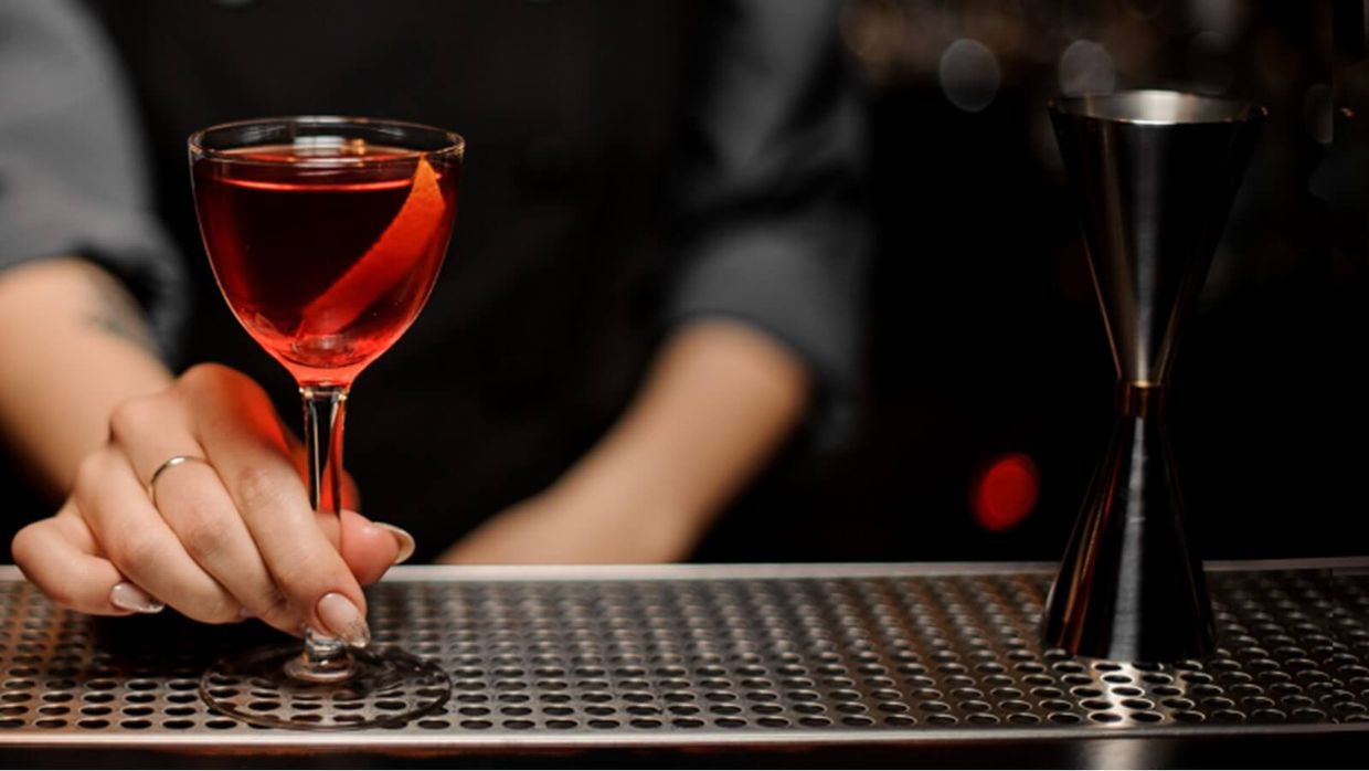 A bartender is holding a glass of red liquid on a bar.