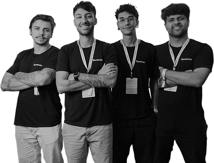 Quatro jovens de braços cruzados, vestindo camisas pretas e cordões, sorrindo para a câmera.