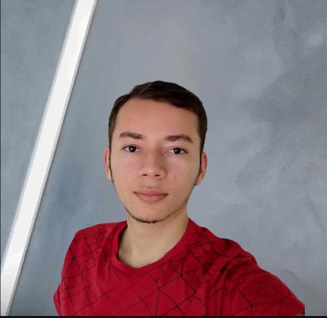 Jovem de camisa vermelha, cabelo castanho, olhando para a câmera contra uma parede azul com luz branca.