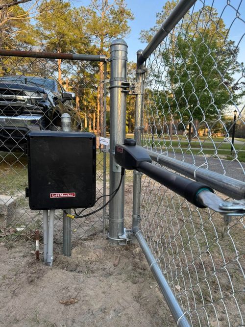 Chain-link gate with black lock box and metal post in a fenced outdoor area.