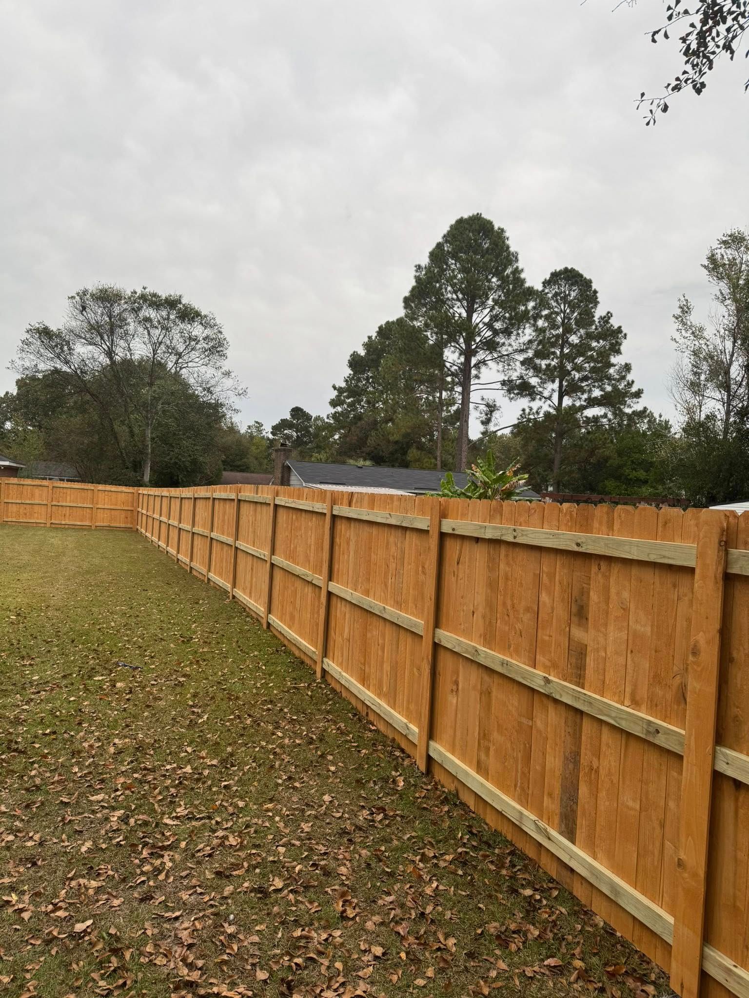Long wooden fence along a grassy yard under a cloudy sky