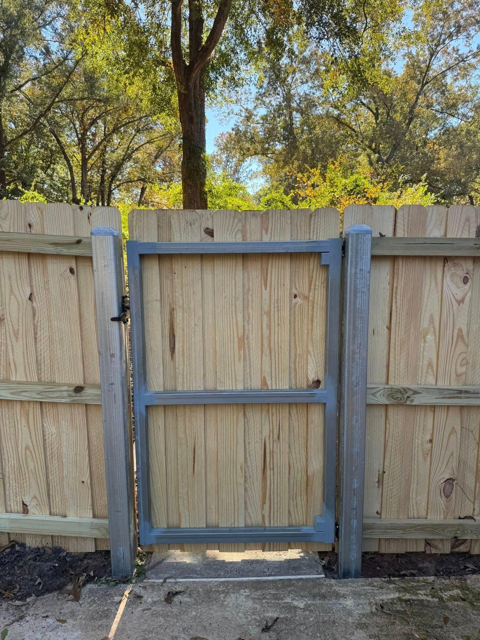 Wooden backyard gate with a gray metal frame set in a tan privacy fence.