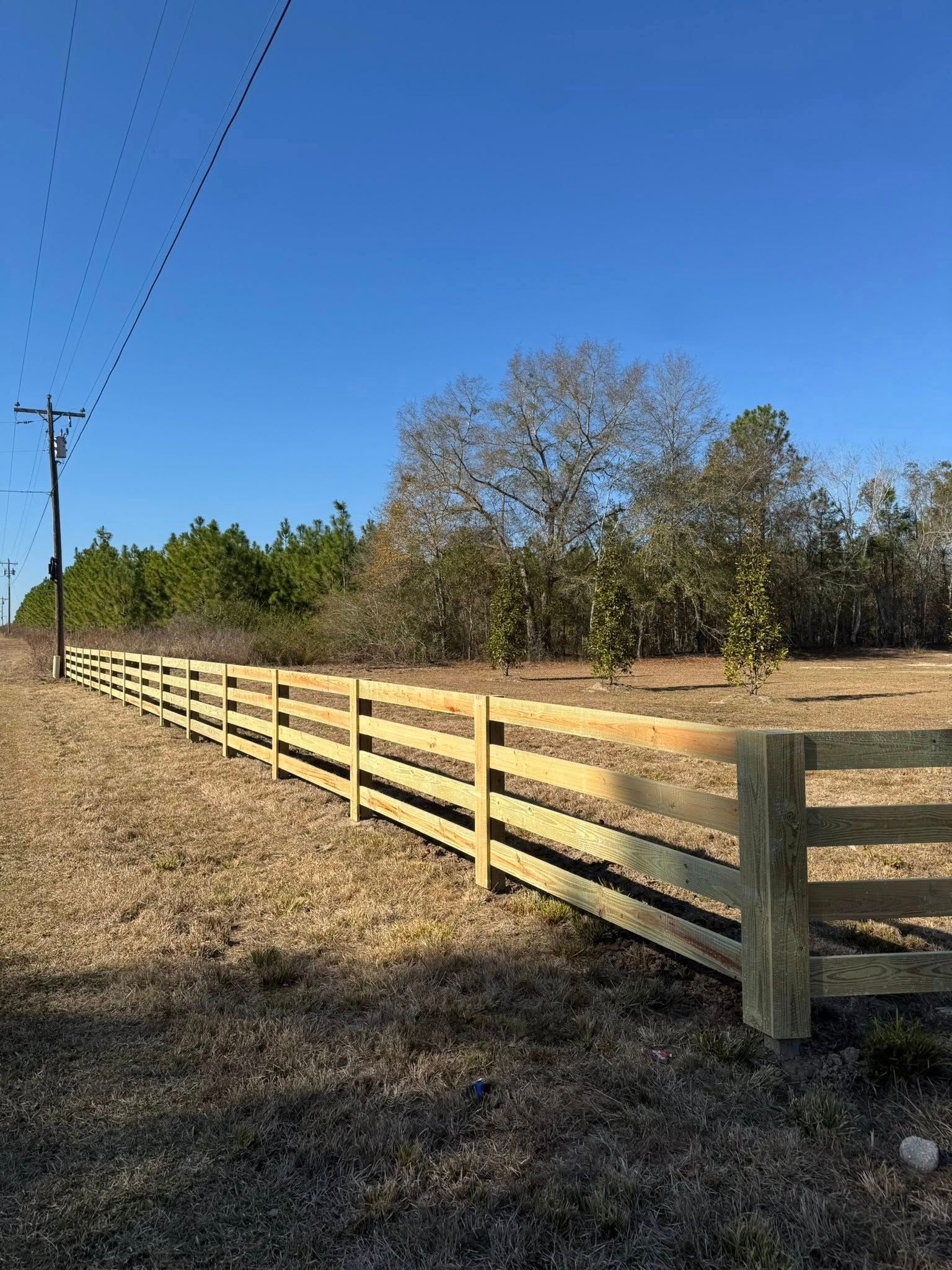 Long wooden fence along a grassy roadside under a clear blue sky
