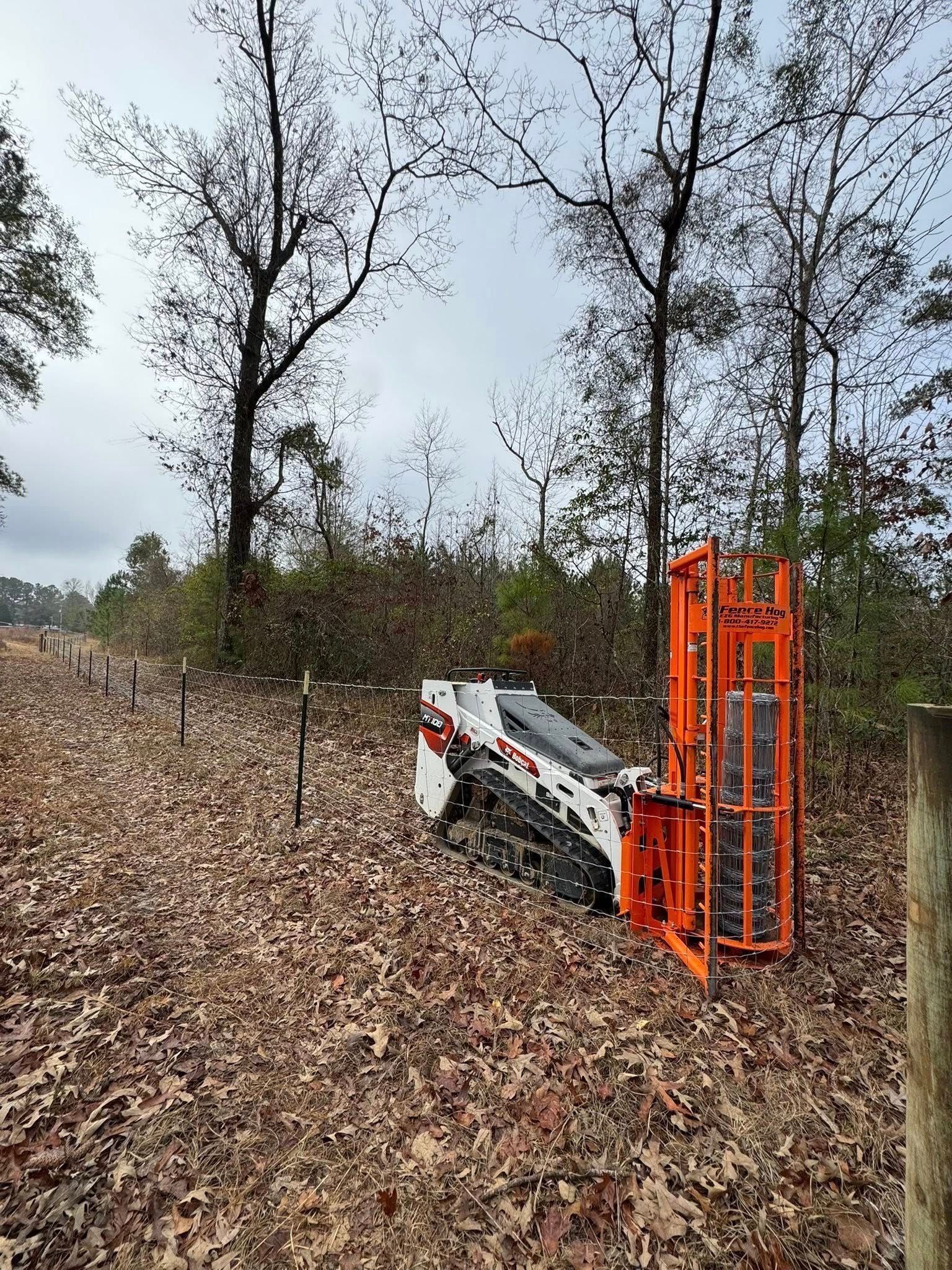 Compact loader on leaf-covered forest floor beside orange metal rack in wooded area
