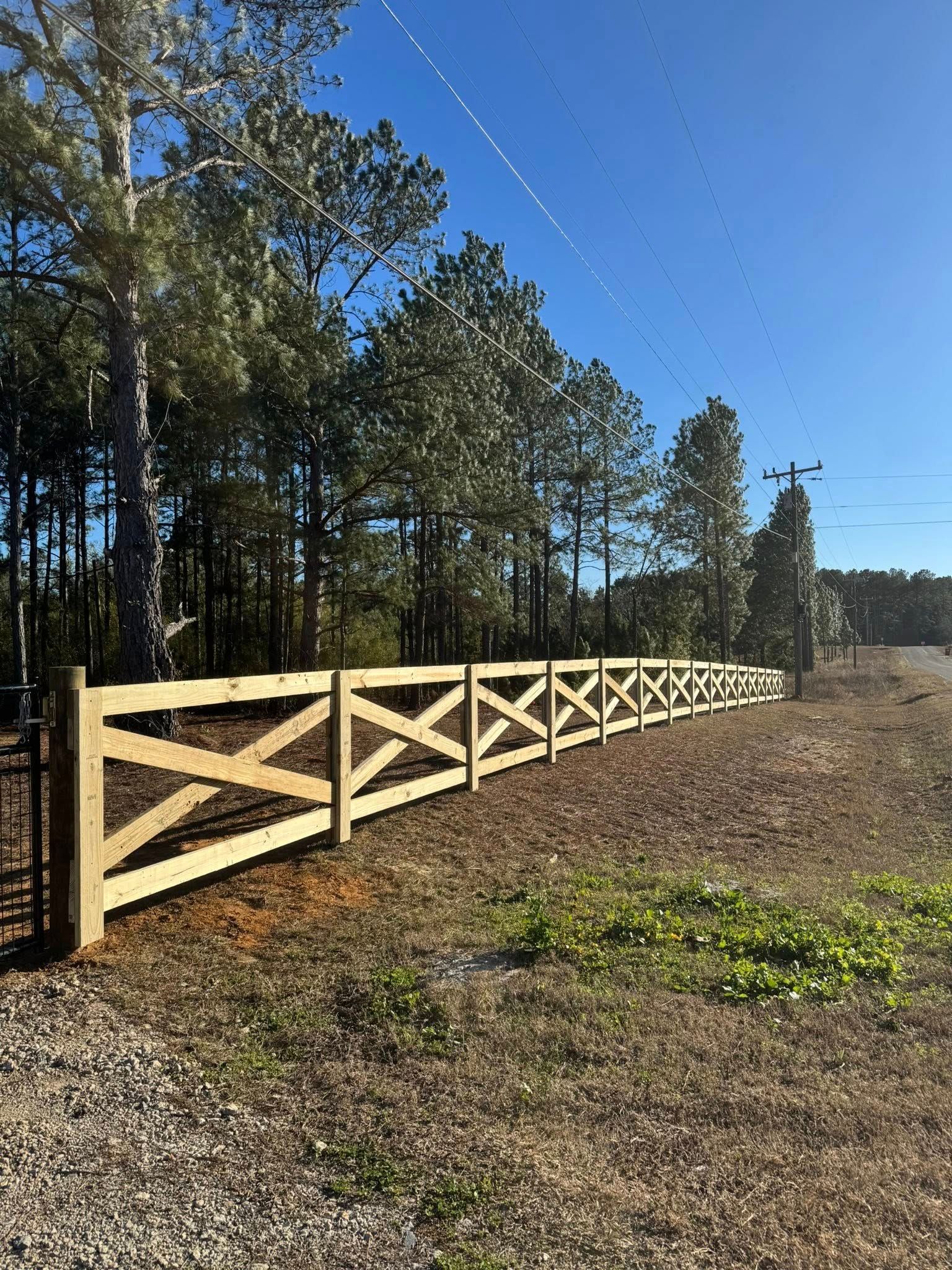 Wooden fence along a wooded field under a clear blue sky