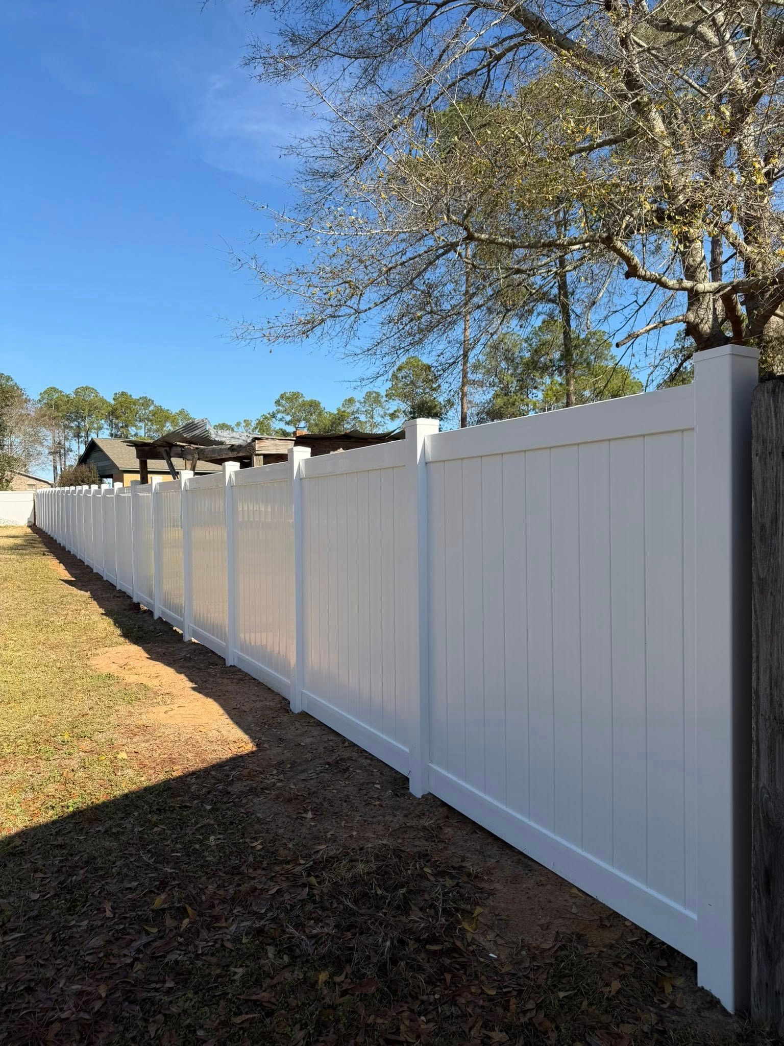 Long white vinyl fence along a yard beside a gravel path under a blue sky