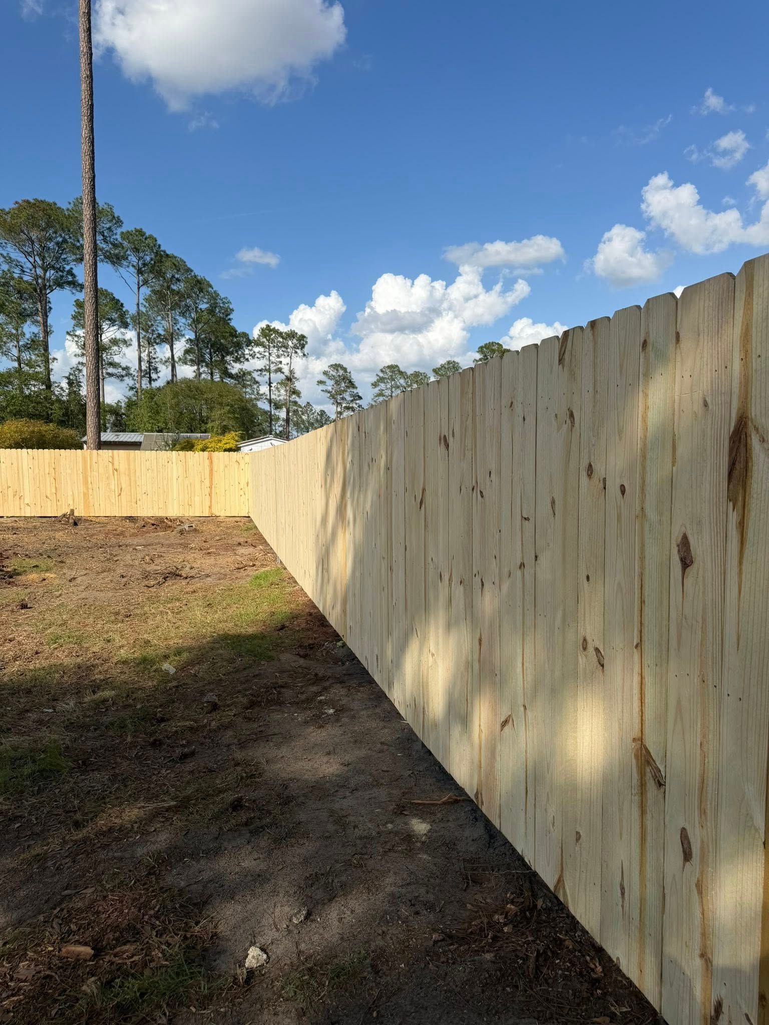 Wooden privacy fence along a dirt yard under a blue sky with clouds