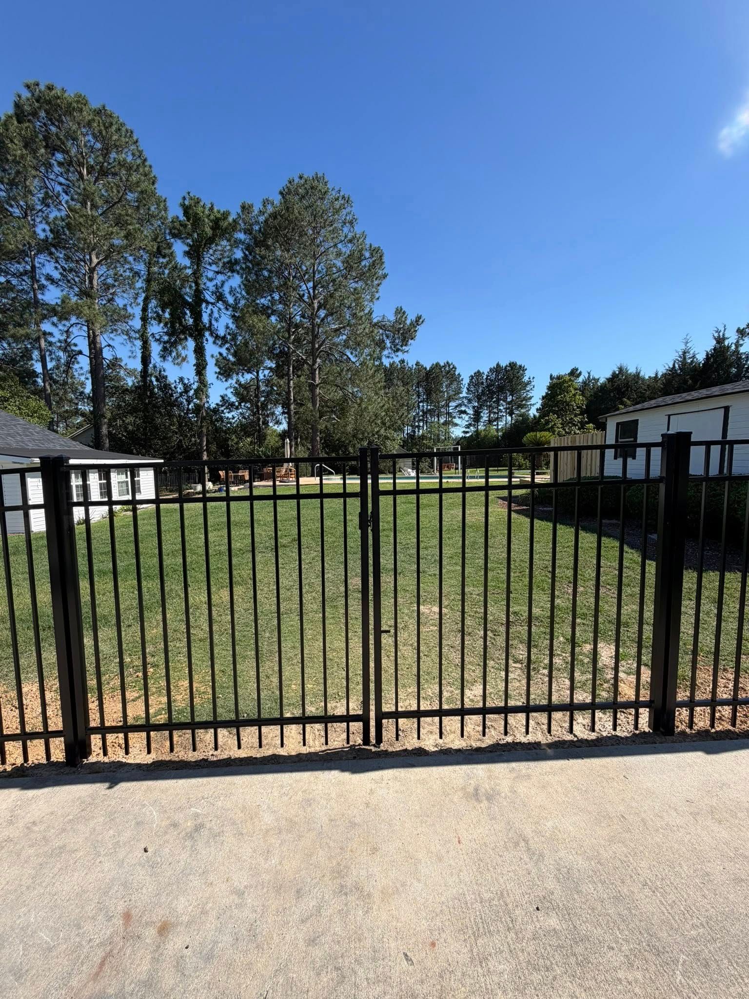 Black metal gate in front of grassy yard with trees and blue sky