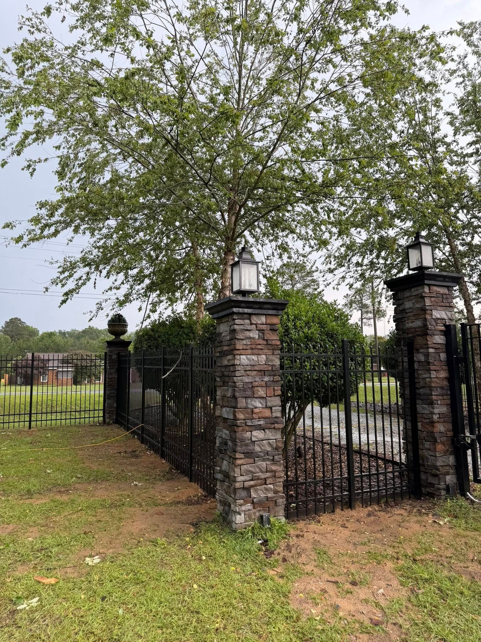 Black iron gate between brick pillars under a large tree beside a grassy path