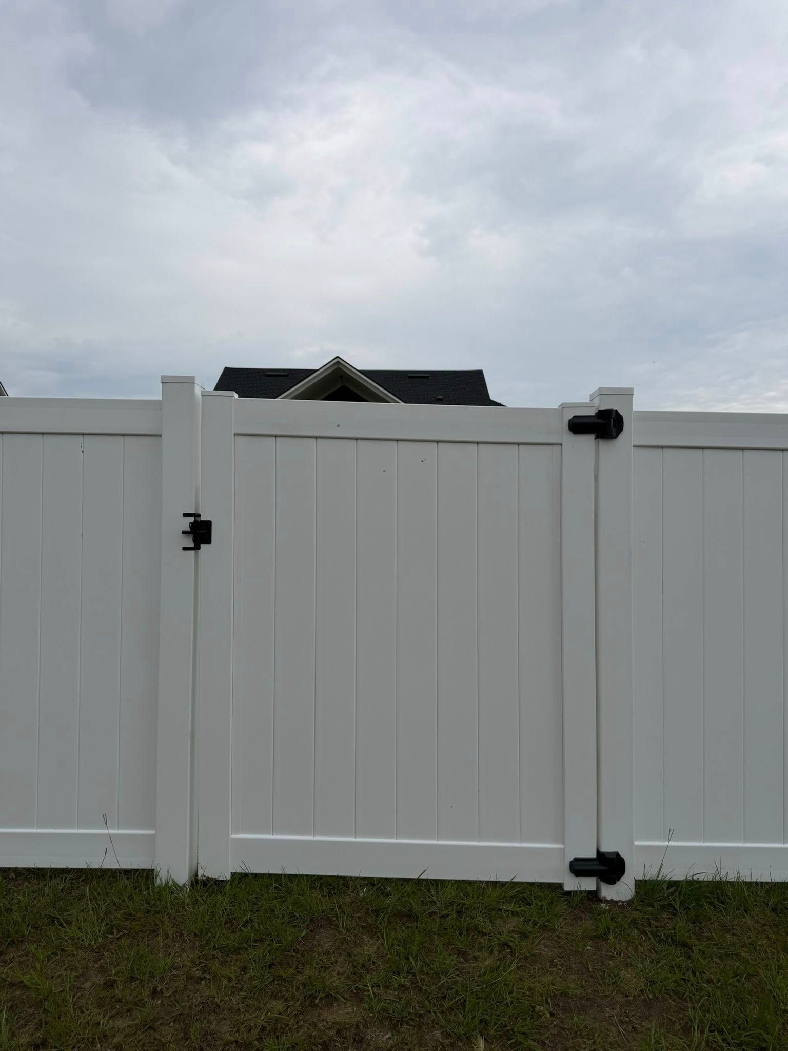 White vinyl fence gate with black hinges and latch under a cloudy sky.