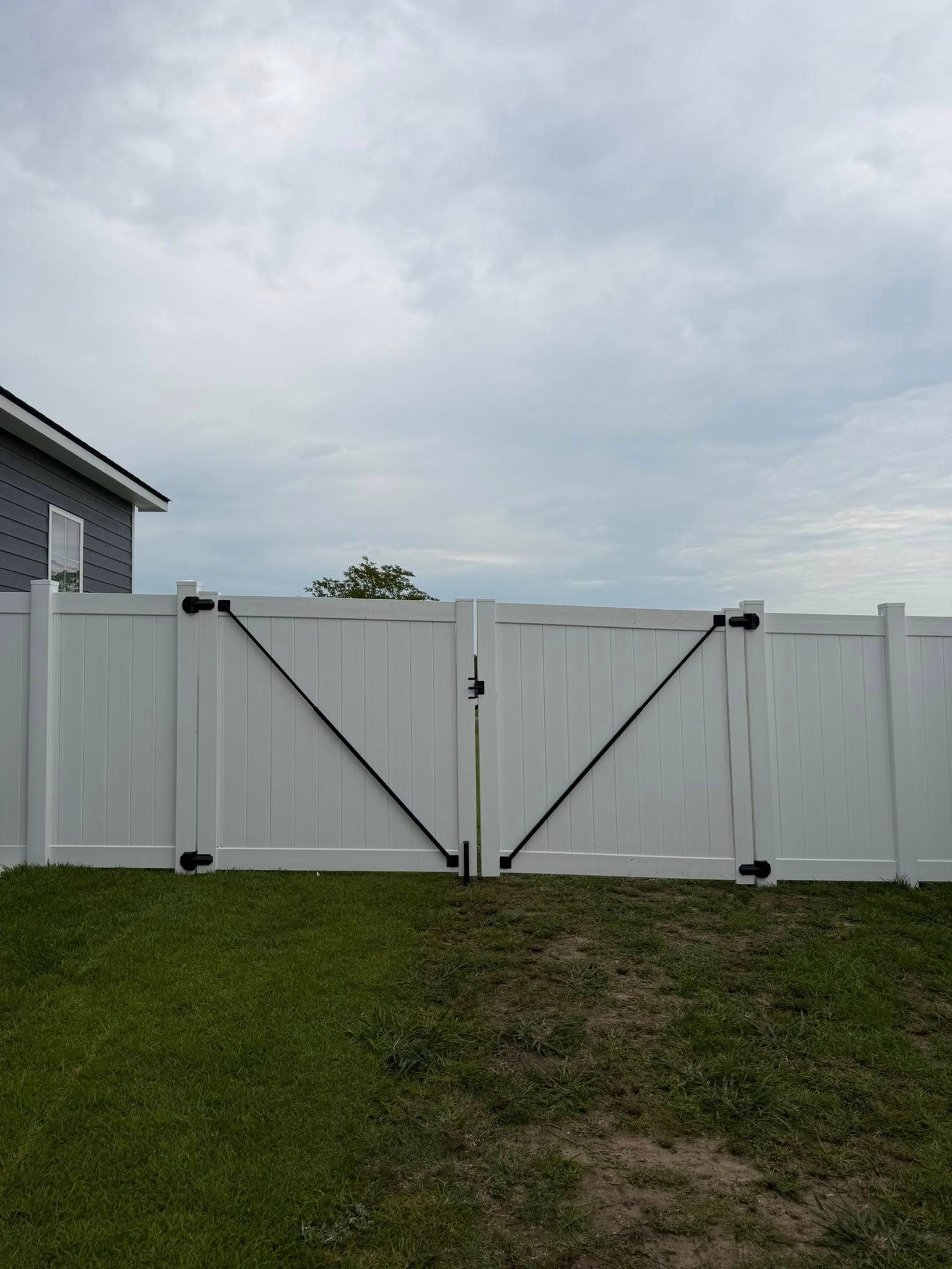 White double gate in a fenced backyard with green grass and cloudy sky