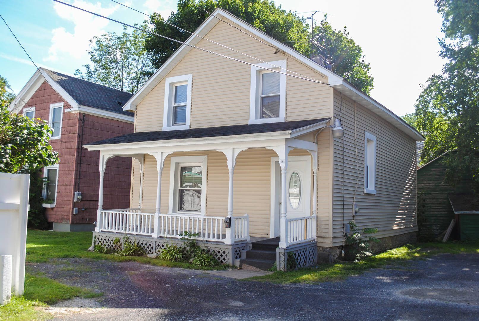 A small house with a porch and a brick house in the background