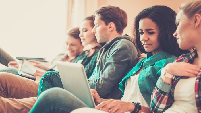 A group of young people are sitting in a row using laptops.