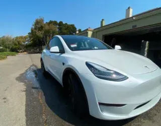 a white tesla model y is parked in front of a garage .