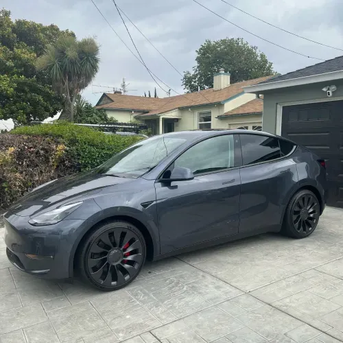 a tesla model y is parked in a driveway in front of a house .