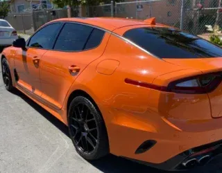 a bright orange car is parked on the side of the road .