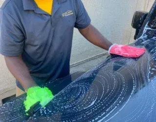 a man is washing a car with a sponge and gloves .