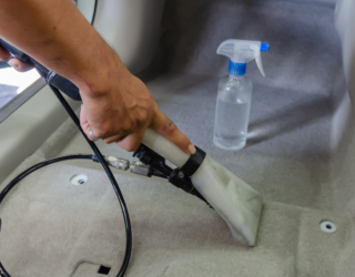 a person is cleaning the carpet of a car with a vacuum cleaner .