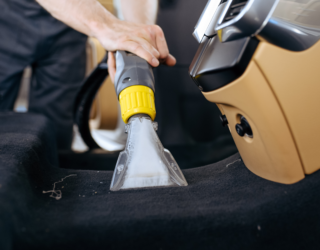 a person is using a vacuum cleaner to clean the carpet in a car .