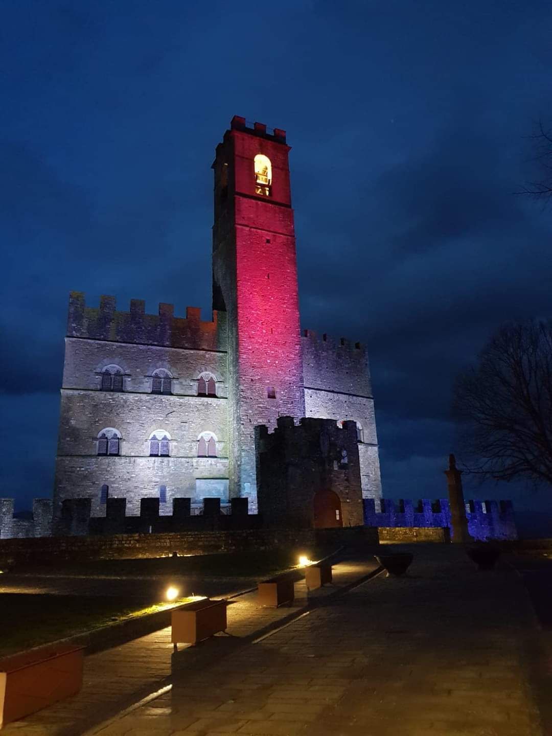Torre di pietra illuminata di notte, con luci rosse e bianche che si stagliano contro un cielo blu scuro.