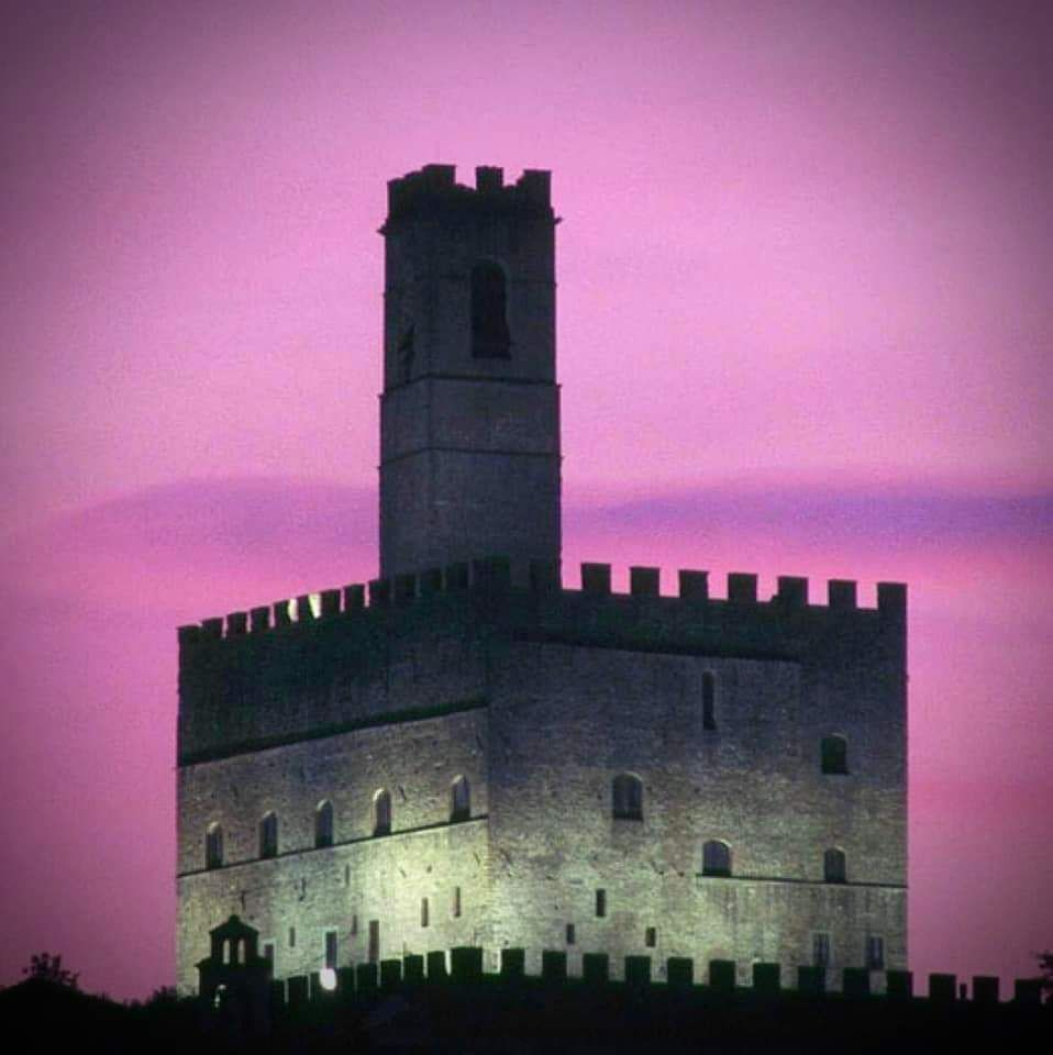 La torre di pietra del castello si staglia contro un cielo al tramonto rosa-violaceo.