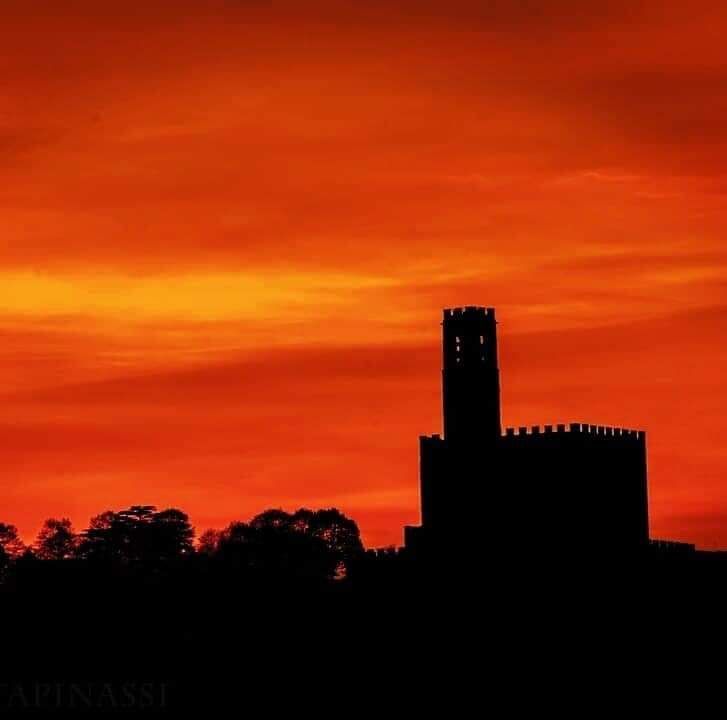 Silhouette di una torre di castello contro un cielo al tramonto dai colori vivaci, arancioni e rossi.