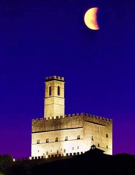 Torre di un castello di pietra illuminata sotto una luna crescente in un cielo notturno blu scuro