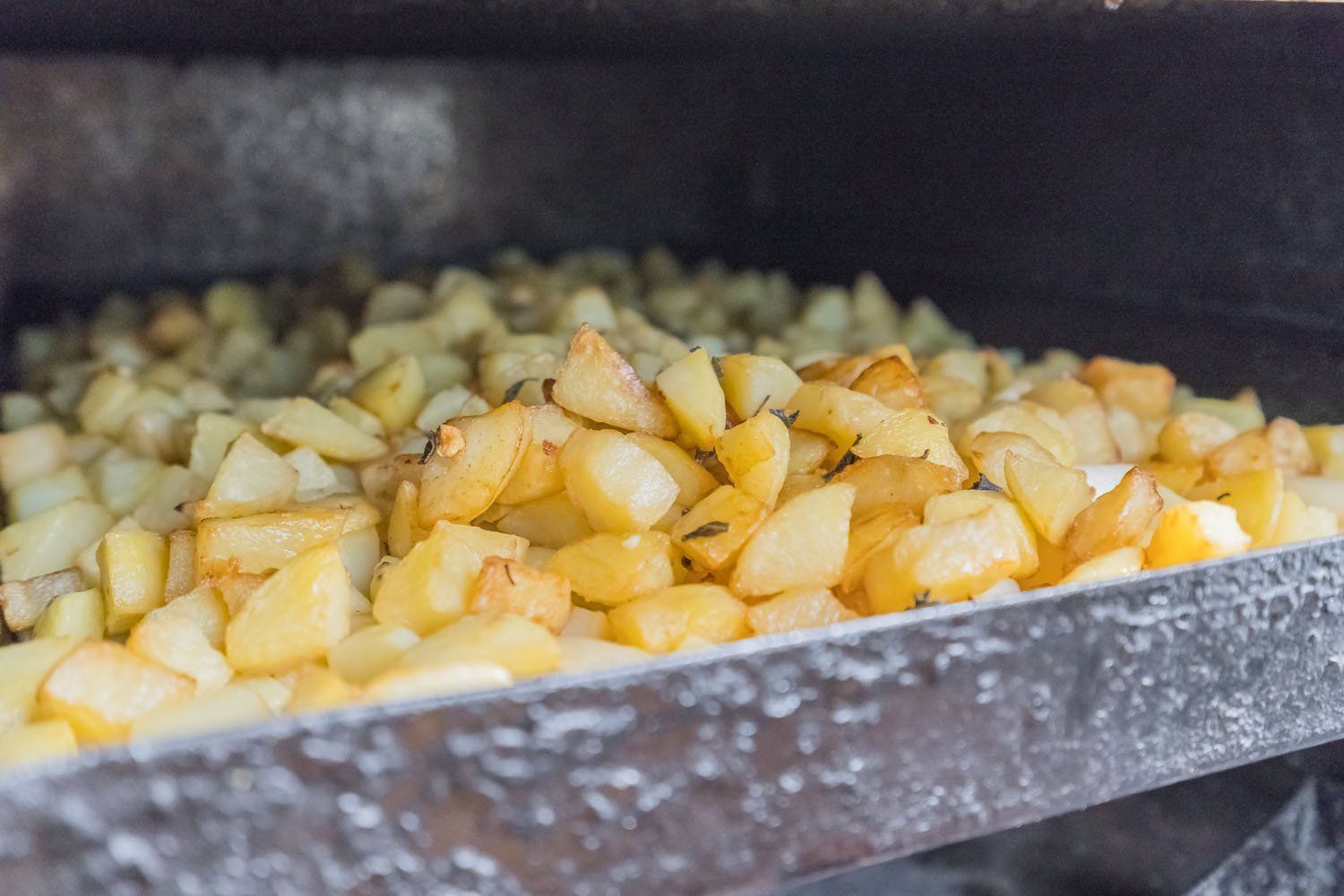 Una teglia di patate a cubetti che cuociono in forno, con pezzi dorati sparsi su una teglia da forno.
