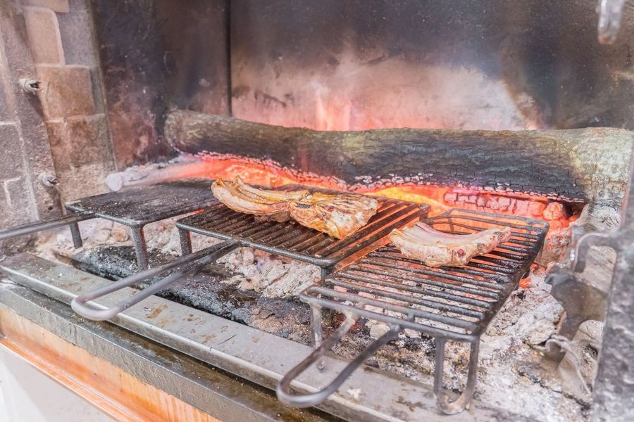Bistecche e salsicce grigliate su una griglia metallica all'interno di un camino in mattoni, su fiamme libere.