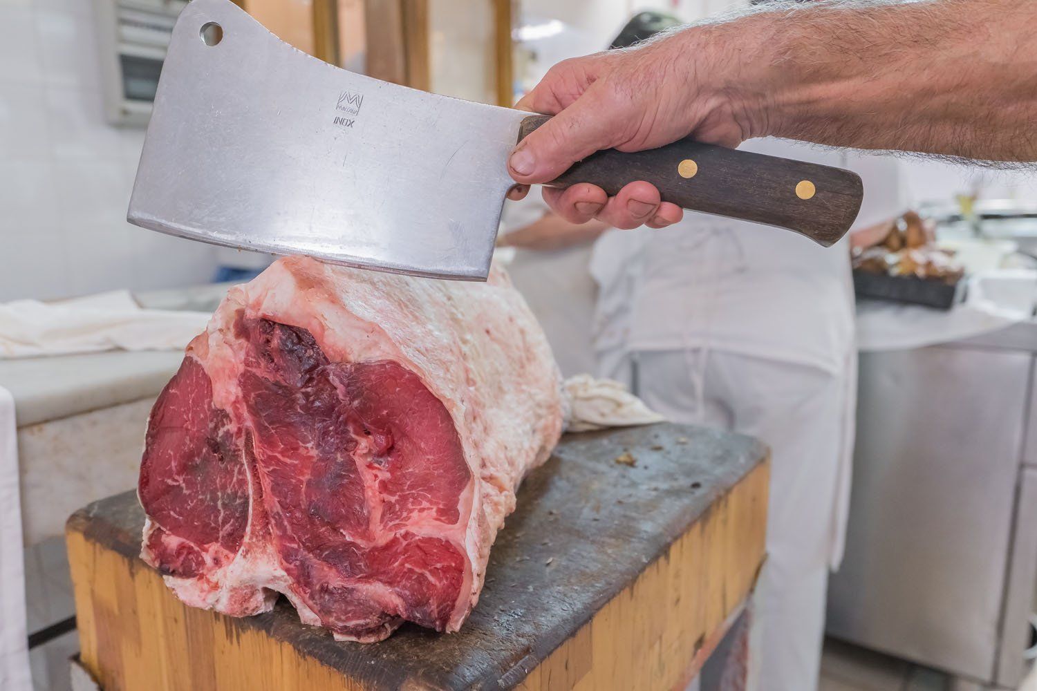 Un macellaio taglia un grosso pezzo di carne cruda su un ceppo di legno con una mannaia.