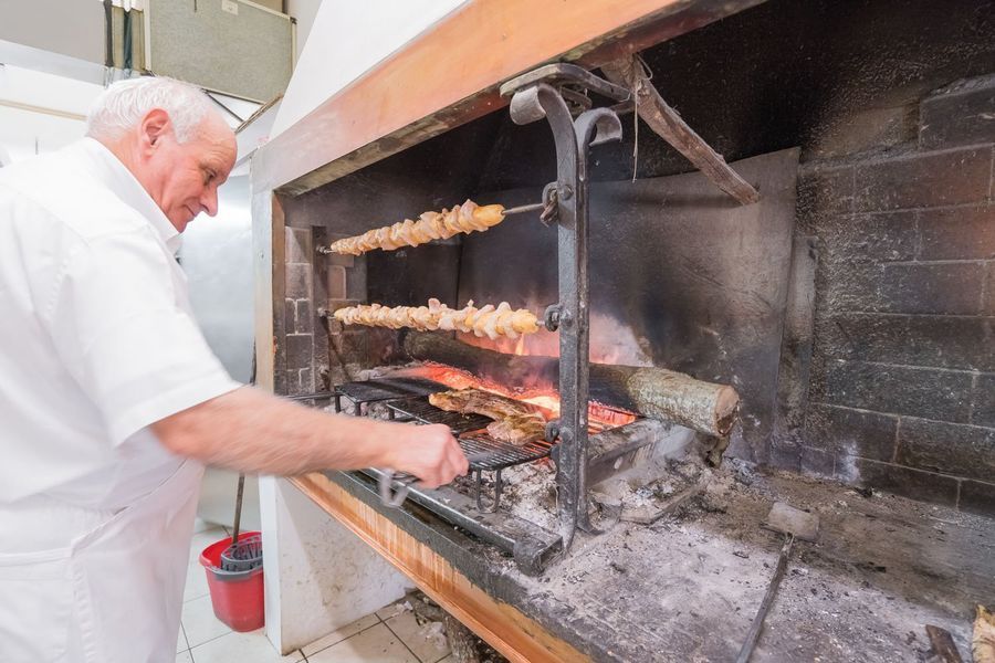 Lo chef controlla gli spiedini su una grande griglia a legna in una cucina piena di fumo.