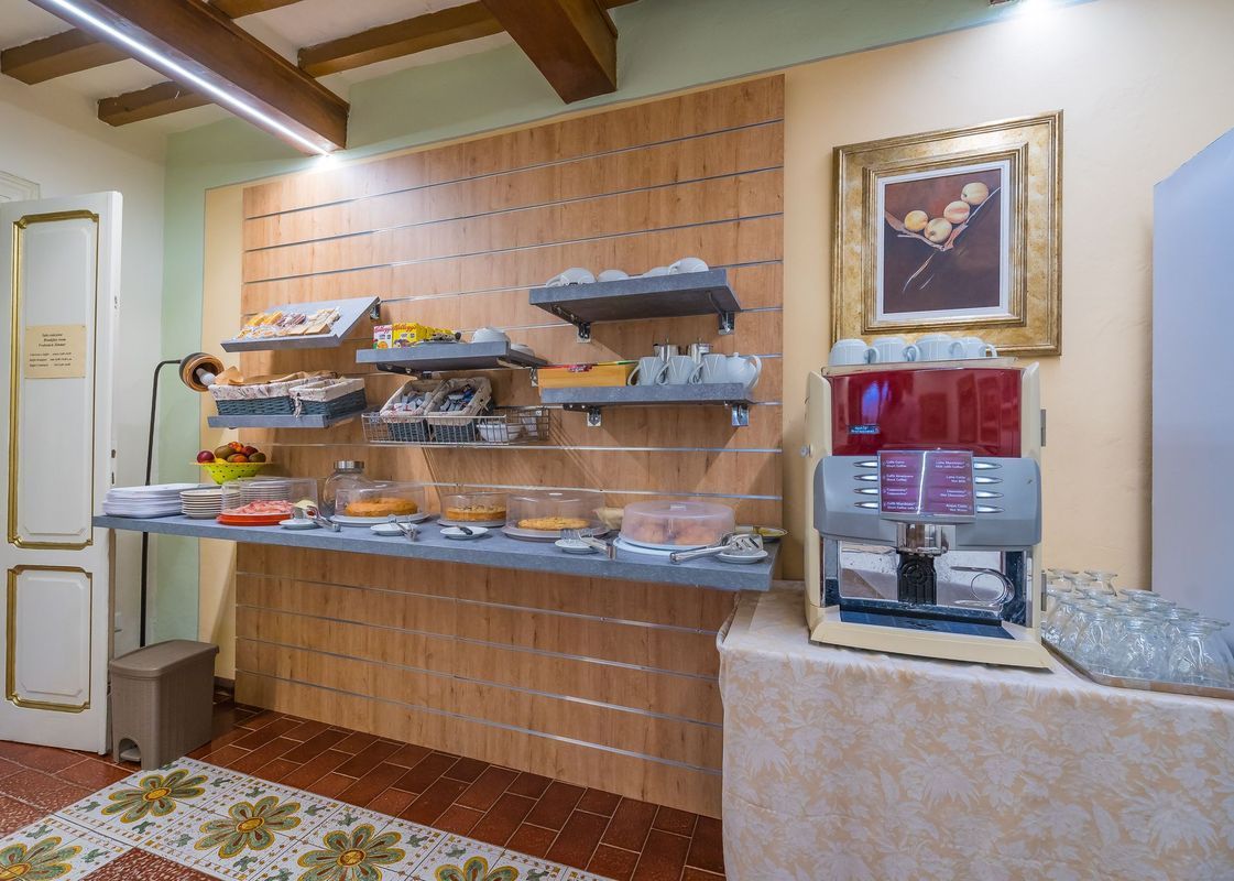 Tavolo da buffet con pasticcini e frutta, oltre a un distributore di bevande, in una luminosa sala da pranzo.