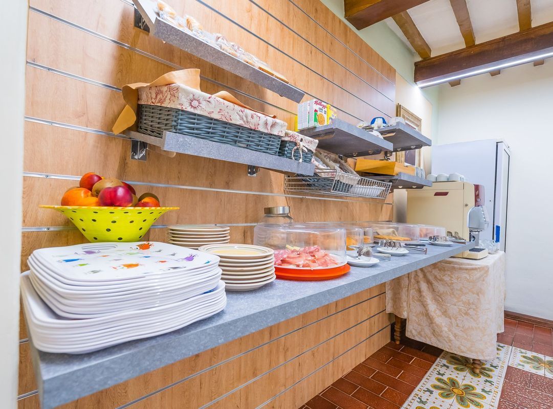 Tavolo da buffet con piatti impilati, fruttiera e piatti coperti in una luminosa sala da pranzo.