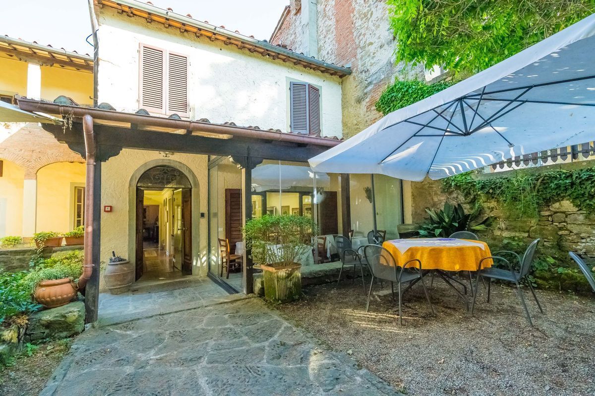 Cortile con patio, portale ad arco, muri in pietra e tavolo sotto un grande ombrellone bianco.
