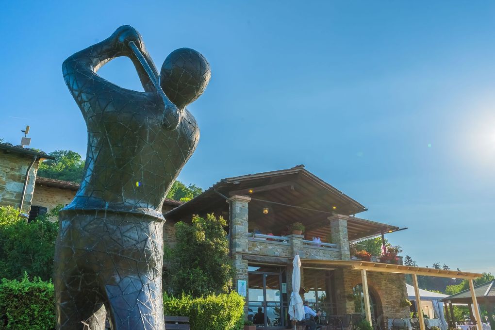 Statua di bronzo di un golfista in un giardino verdeggiante accanto a una casa rustica sotto un cielo azzurro brillante.