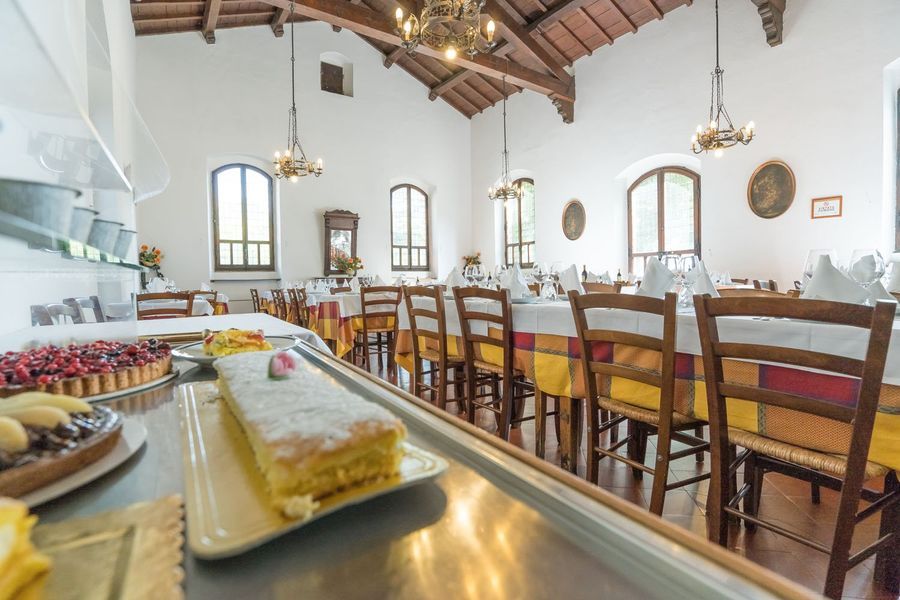 Luminosa sala da pranzo con lunghi tavoli in legno, sedie, lampadari e un bancone buffet in primo piano.