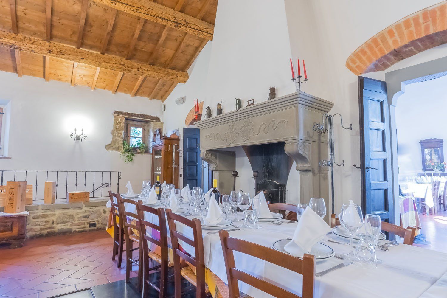 Elegante sala da pranzo con lungo tavolo apparecchiato, camino in pietra e alto soffitto in legno.