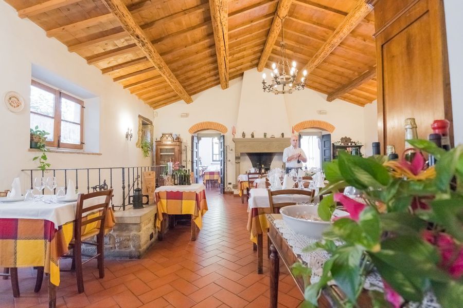 Luminosa sala da pranzo in stile rustico con piastrelle in terracotta, travi a vista sul soffitto e tavoli apparecchiati con tovaglie bianche.