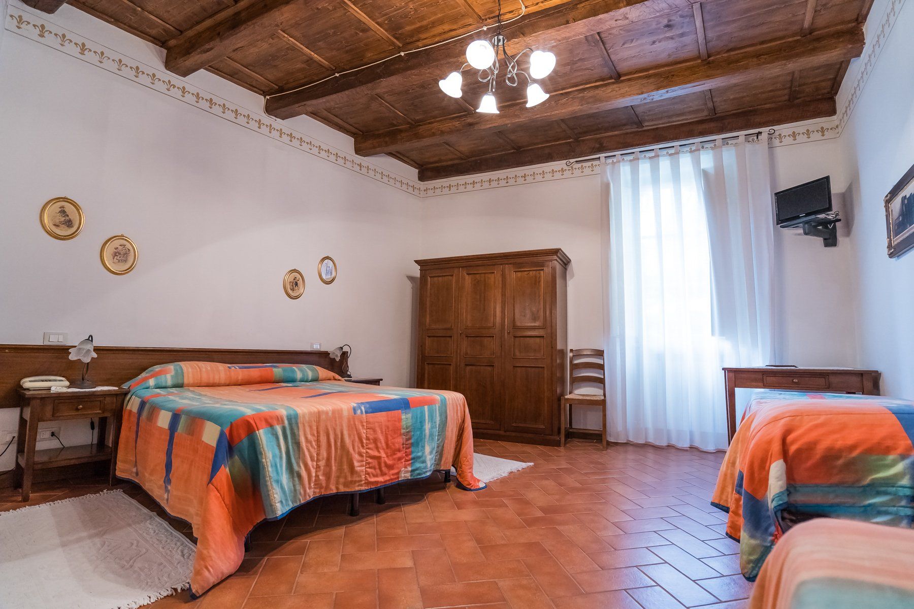 Camera da letto rustica con due letti singoli, armadio in legno, pavimento in piastrelle di terracotta e una finestra luminosa.