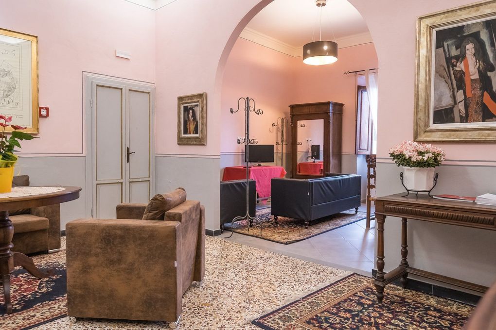 Accogliente salotto rosa con poltrone, tappeto a motivi geometrici, tavolini e quadri incorniciati sotto una porta ad arco.