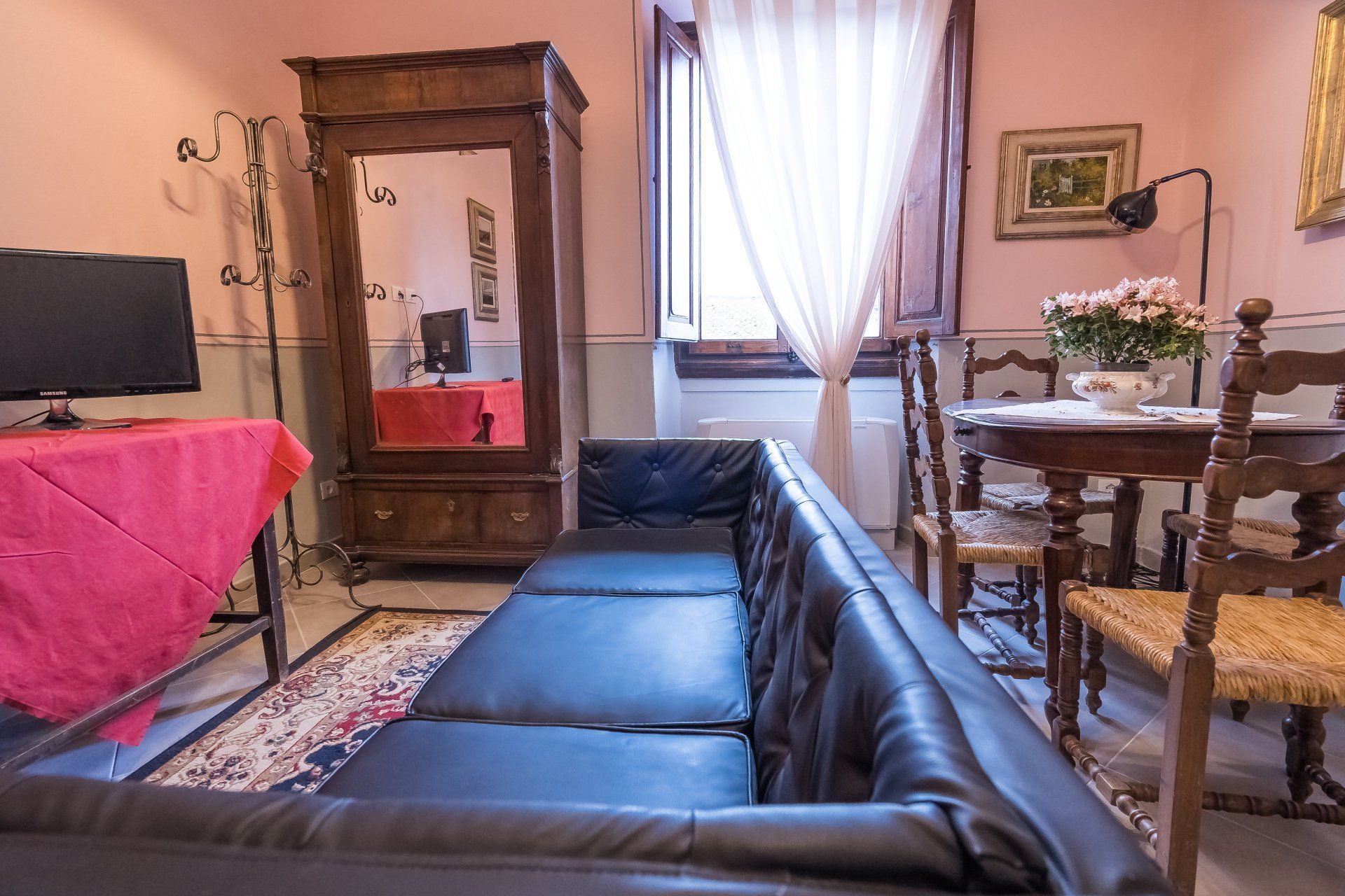 Accogliente soggiorno con divano angolare nero, vetrina in legno, tavolo da pranzo e pareti rosa.