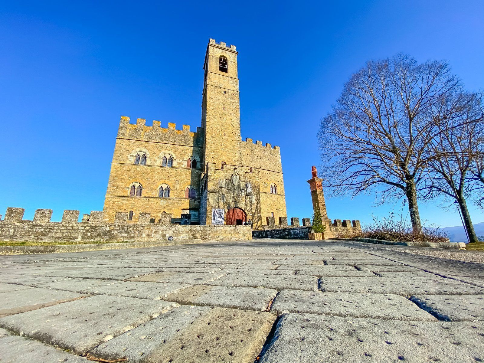 Castello di pietra con un'alta torre su una collina rocciosa sotto un cielo azzurro brillante.
