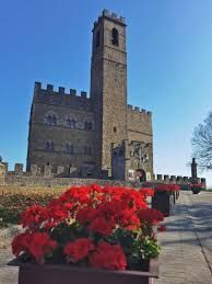 Torre di pietra del castello con fiori rossi in primo piano sotto un cielo azzurro